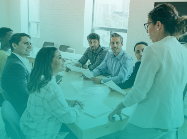 team of people sitting at desk looking at woman presenting