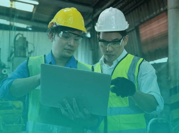 Two manufacturing workers reviewing operations data on a laptop on the plant floor